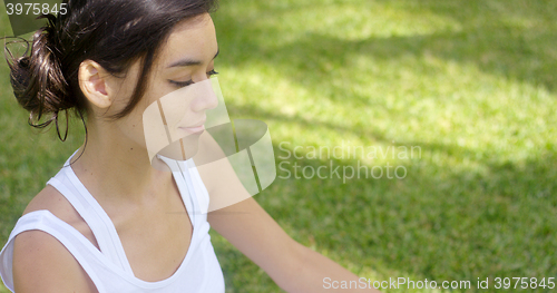 Image of Serene young woman meditating on a green lawn