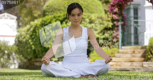 Image of Young woman sitting meditating in a garden