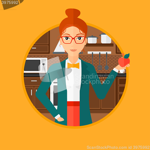 Image of Young woman with apple in the kitchen.