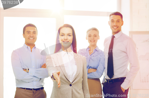 Image of smiling businesswoman in office with team on back