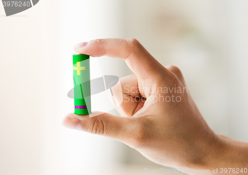 Image of close up of hand holding green alkaline battery