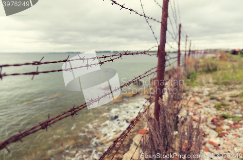Image of barb wire fence over gray sky and sea