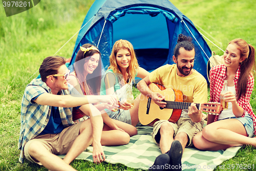 Image of happy friends with drinks and guitar at camping