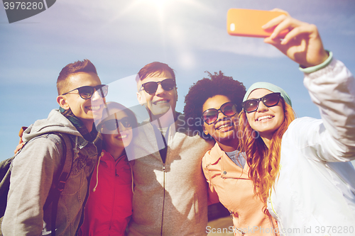 Image of smiling friends taking selfie with smartphone