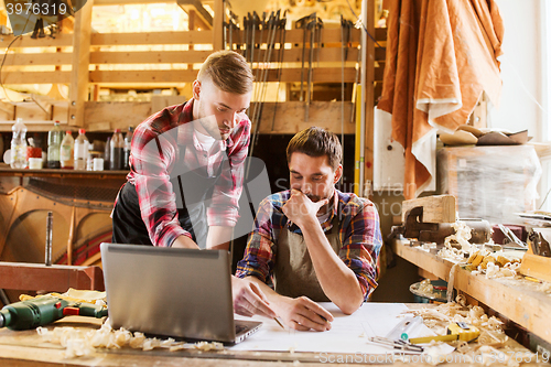 Image of carpenters with laptop and blueprint at workshop