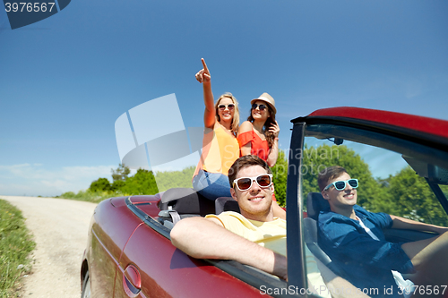 Image of happy friends driving in cabriolet car at country