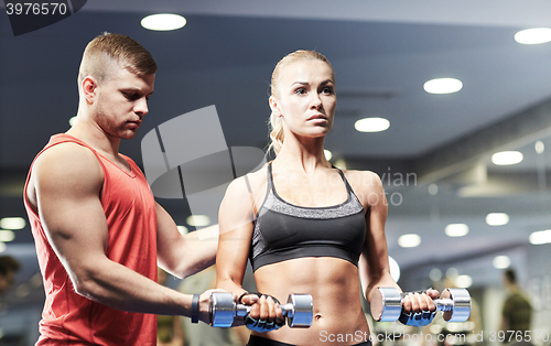 Image of young couple with dumbbells flexing muscles in gym