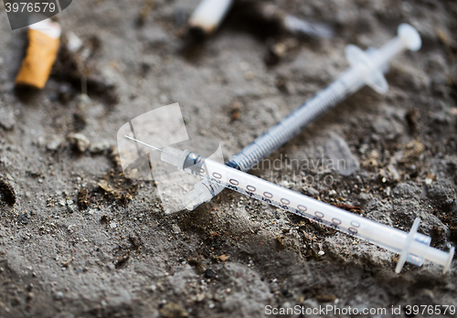 Image of close up of syringe and smoked cigarette on ground