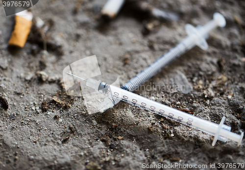Image of close up of syringe and smoked cigarette on ground