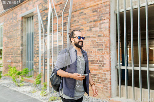 Image of man with earphones and smartphone walking in city