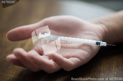 Image of close up of addict hand and used drug syringe