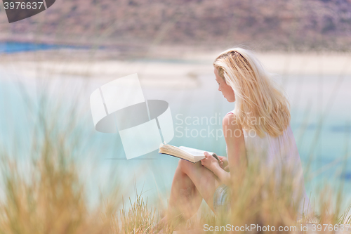 Image of Woman reading book, enjoying sun on beach.