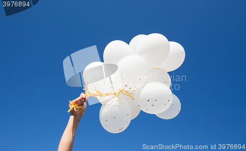 Image of close up of hand with white balloons in blue sky