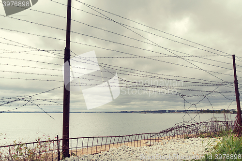 Image of barb wire fence over gray sky and sea