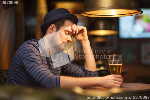 Image of unhappy lonely man drinking beer at bar or pub