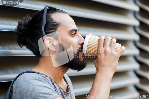 Image of man drinking coffee from paper cup on street