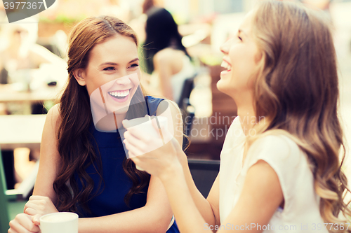 Image of smiling young women with coffee cups at cafe