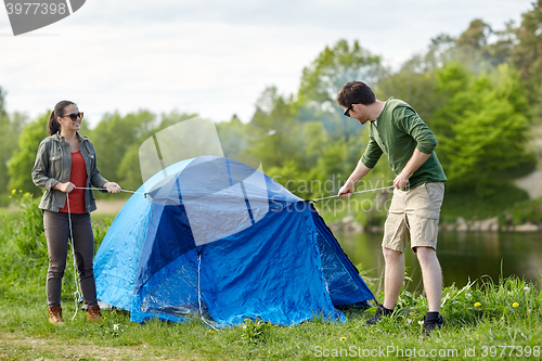 Image of happy couple setting up tent outdoors