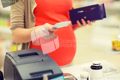 Image of pregnant woman with money at cashbox in drugstore