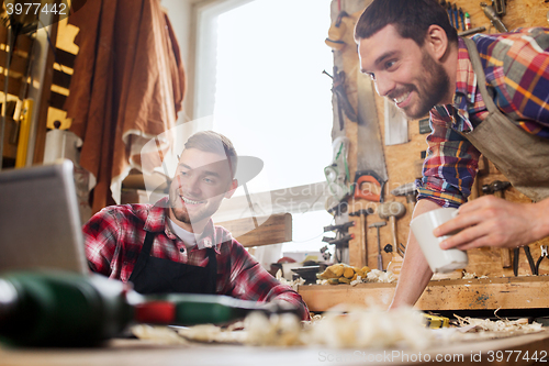 Image of two smiling carpenters with laptop at workshop