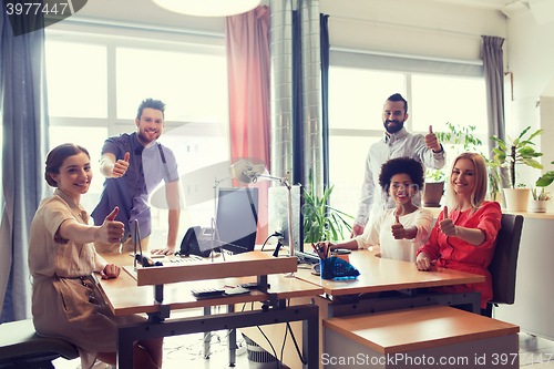 Image of happy creative team showing thumbs up in office