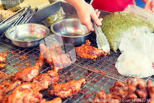 Image of close up of cook hand with tongs grilling chicken