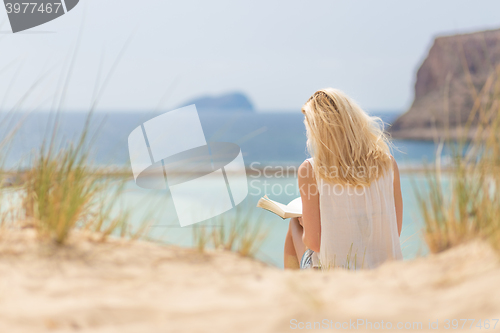 Image of Woman reading book, enjoying sun on beach.