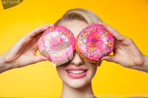 Image of Short-haired model covering eyes behind two pink donuts