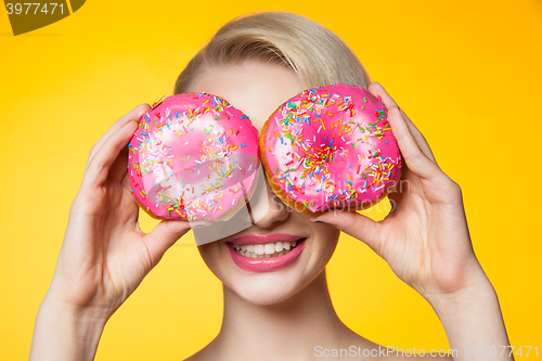 Image of Short-haired model covering eyes behind two pink donuts