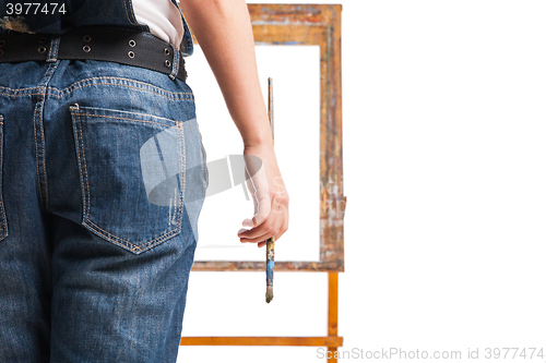 Image of Young smiling woman painter with paintbrush standing at easel 