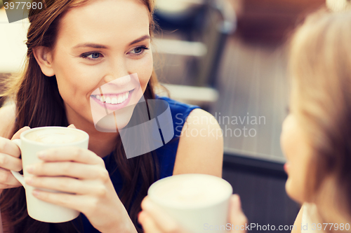 Image of smiling young women with coffee cups at cafe