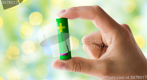 Image of close up of hand holding green alkaline battery