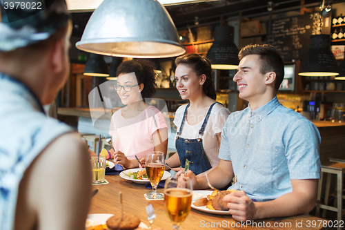 Image of happy friends eating and drinking at bar or pub