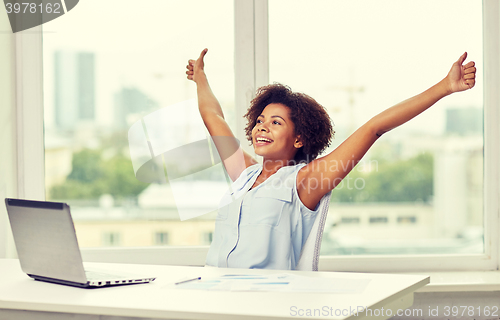 Image of happy african woman with laptop at office