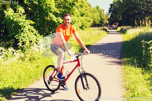 Image of happy young man riding bicycle outdoors