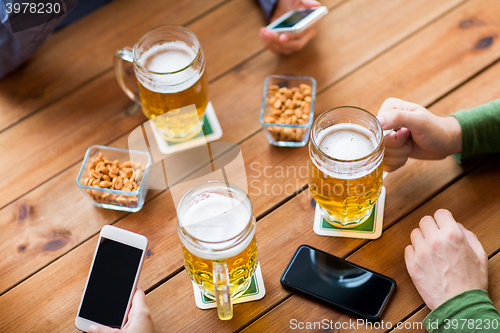 Image of close up of hands with smartphones and beer at bar