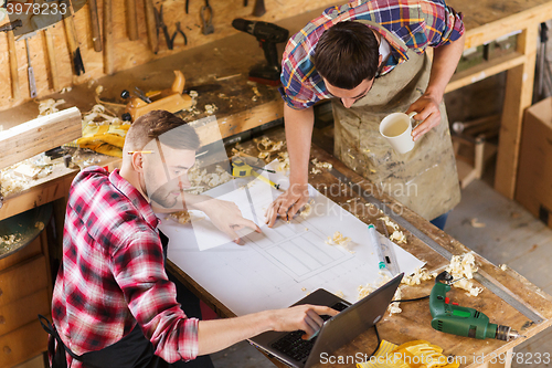 Image of carpenters with laptop and blueprint at workshop