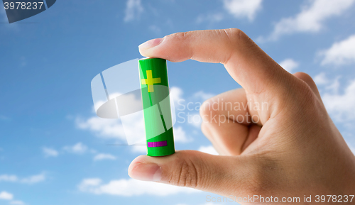 Image of close up of hand holding green alkaline battery