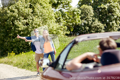 Image of couple hitchhiking and stopping car on countryside