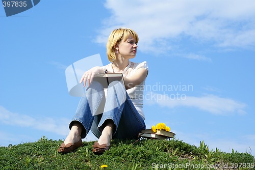 Image of female student outdoor on gren grass with books and blue sky on