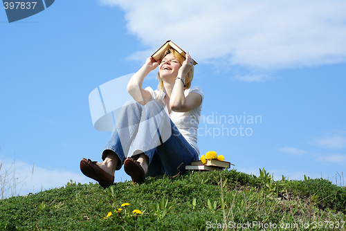 Image of female student outdoor on gren grass with books and blue sky on