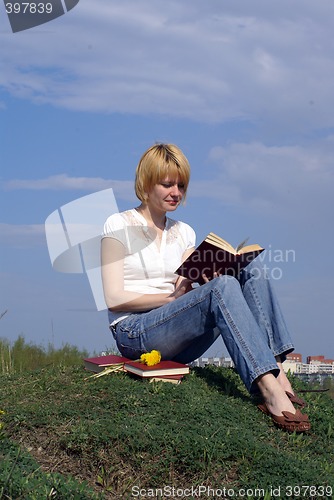 Image of female student outdoor on gren grass with books and blue sky on