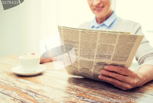 Image of senior woman with coffee reading newspaper at home