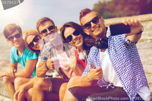 Image of group of smiling friends with smartphone outdoors