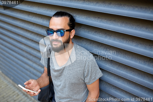 Image of man with backpack texting on smartphone in city