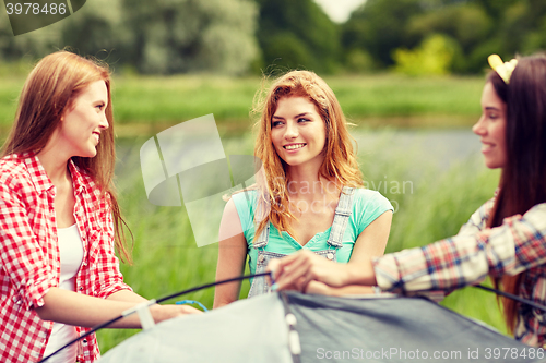 Image of group of smiling friends setting up tent outdoors