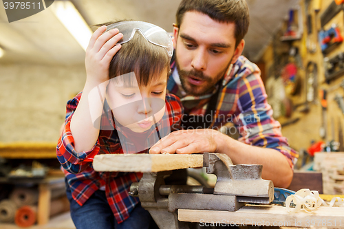 Image of father and little son with wood plank at workshop