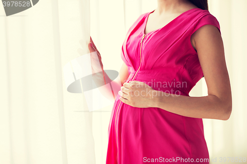 Image of pregnant woman looking through window at home