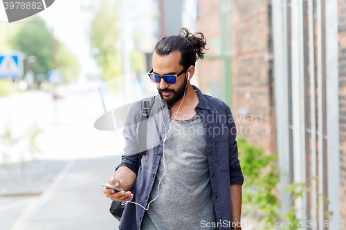 Image of man with earphones and smartphone walking in city