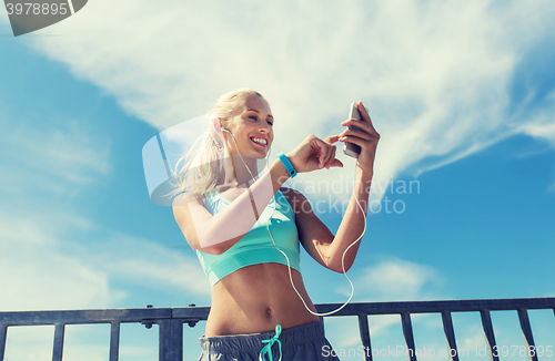 Image of happy woman with smartphone and earphones outdoors